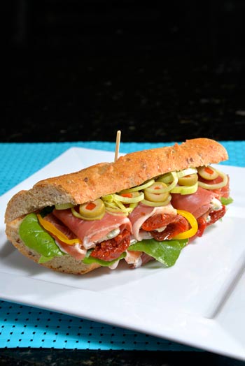 Sandwich de prosciutto, tomate, rucula con queso azul en pan con semillas.